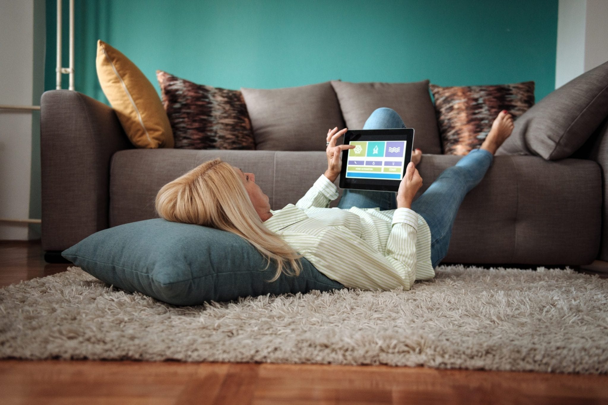 femme alongée qui regarde sa tablette et contrôle les réglages de sa maison